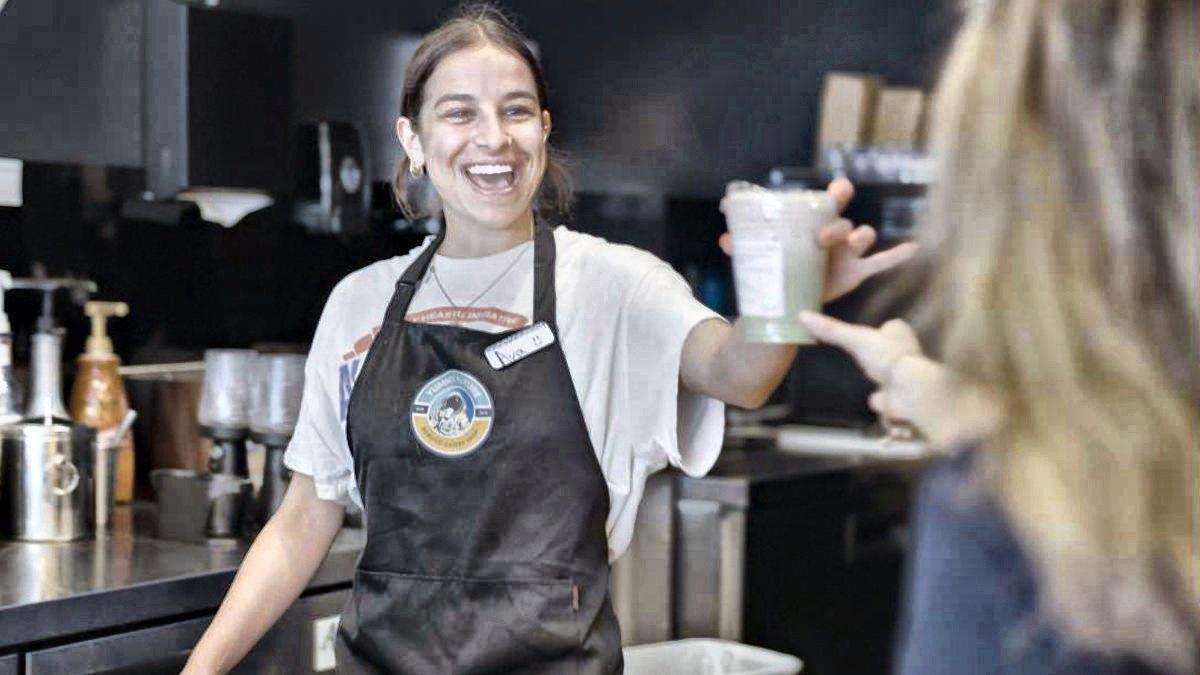 A store lead handing a matcha across the counter to a customer